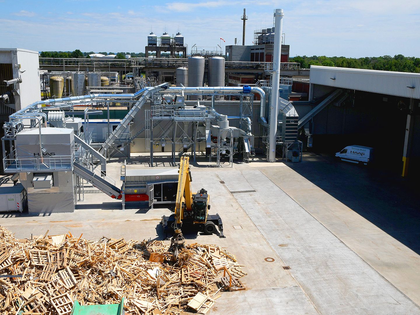 Altholzaufbereitungsanlage mit Bagger Altholzaufbereitungsanlage mit losem Holzlager und Bagger bei der Verarbeitung von Altholz.